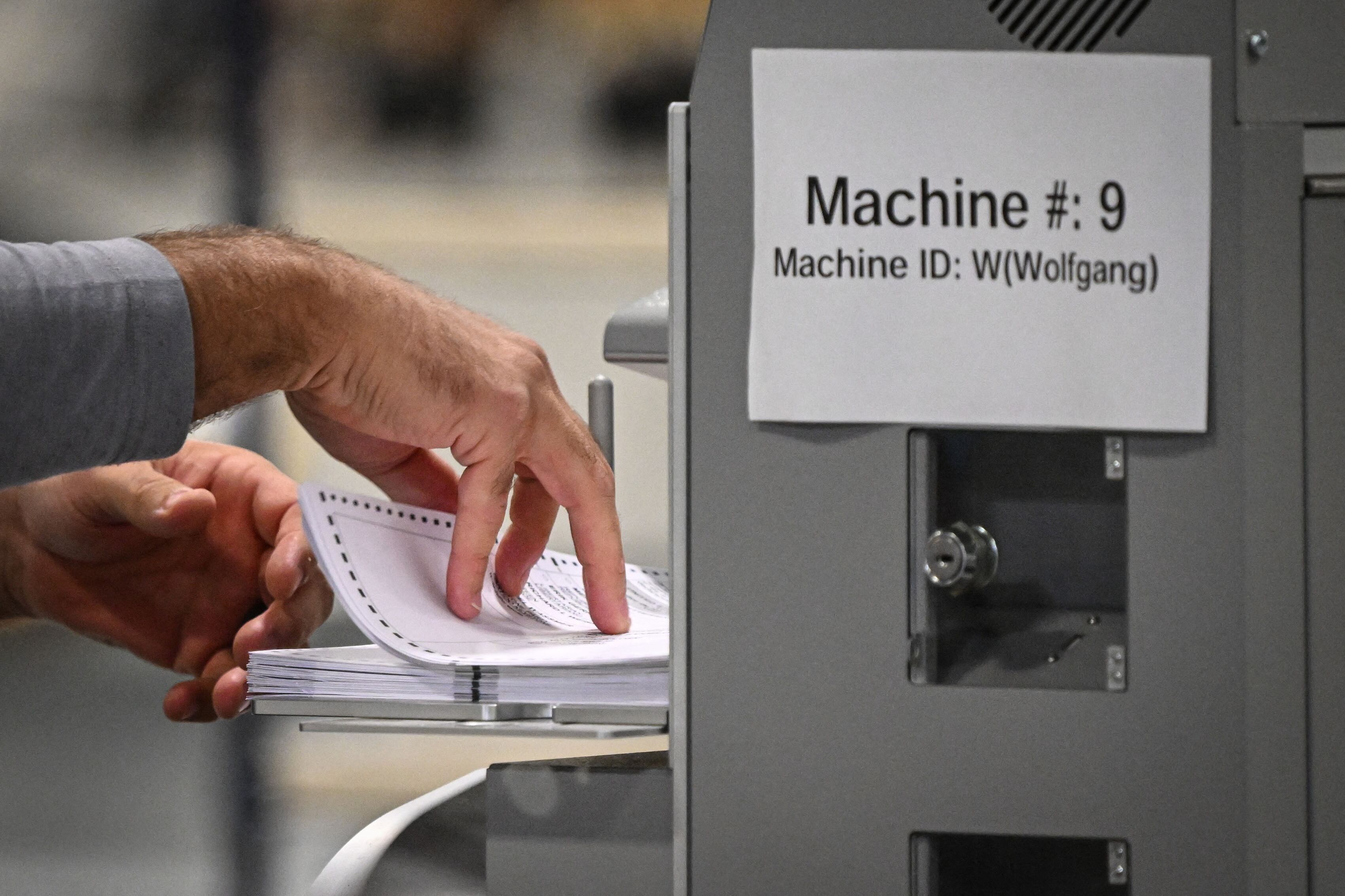 A pair of hands work to sort ballots near a machine.